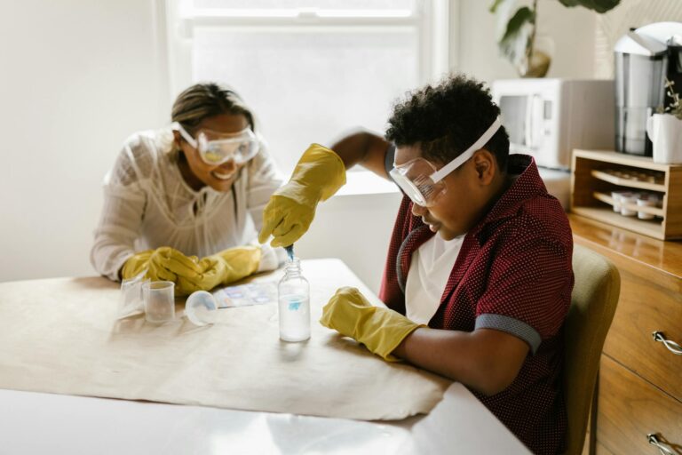 Mother and son wearing goggles and gloves doing a science experiment with a bottle and blue liquid.