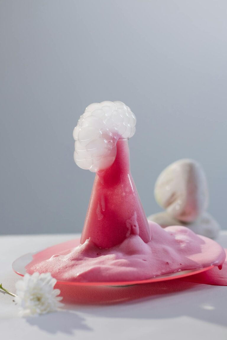 Pink foaming liquid erupting from a glass flask in a scientific experiment.