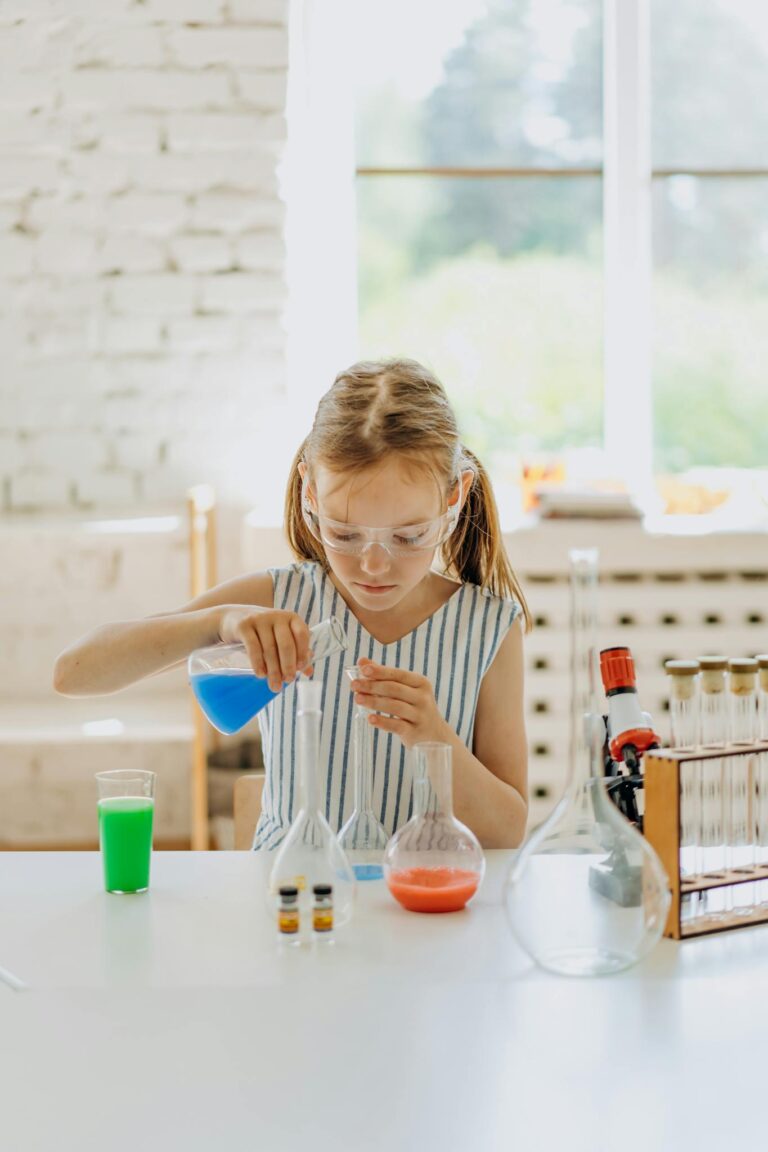 Young girl wearing goggles conducting a science experiment with colorful liquids at a home lab setup.